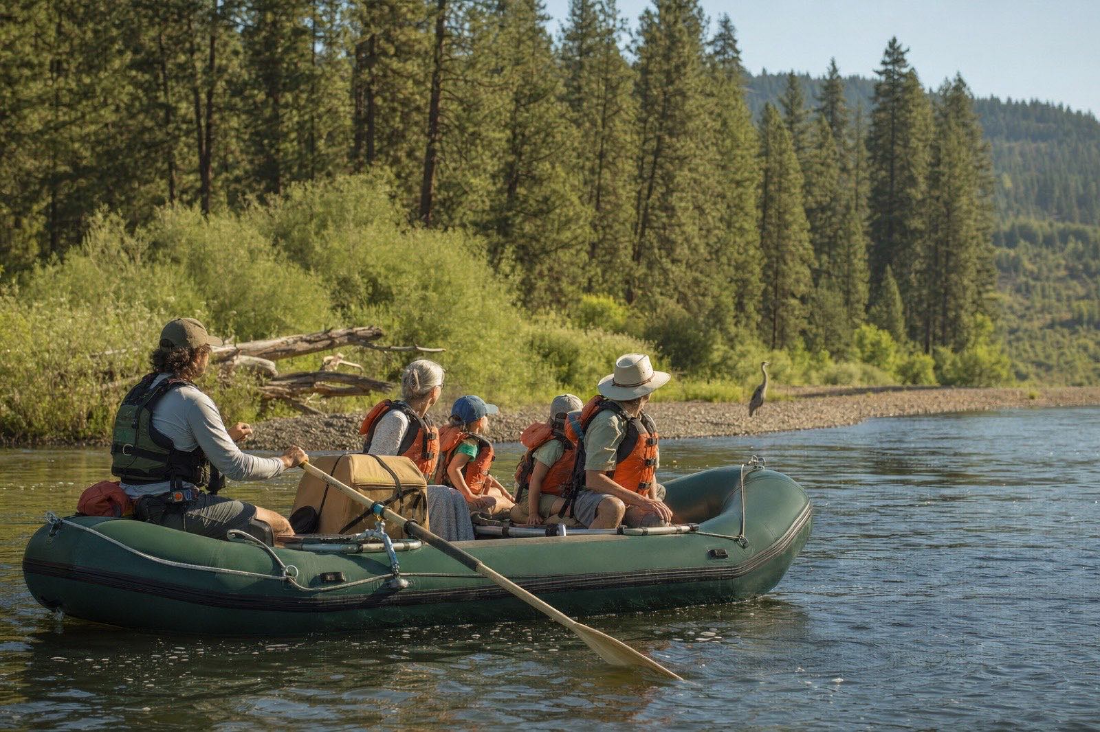 A guide and multigenerational family watching a heron from a calm river raft